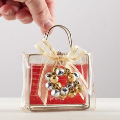 a hand is holding a small christmas ornament in a clear box with gold bells on it