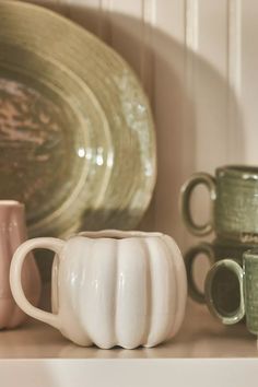 some white and green coffee mugs on a shelf next to other cups, plates and bowls