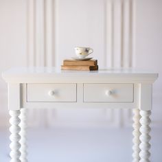 a small white table with two drawers and a cup on top, sitting next to a stack of books