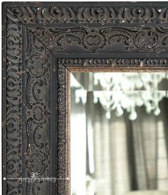 an ornate black framed mirror with a chandelier in the background