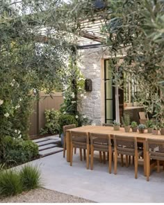 an outdoor dining area with wooden table and chairs, surrounded by greenery on either side