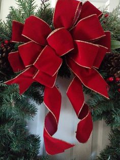 a christmas wreath on the front door with red ribbon and pineconis around it