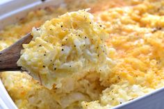 a casserole dish filled with potatoes and topped with a wooden spoon full of cheese