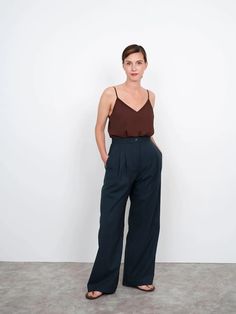 a woman standing in front of a white wall wearing dark blue pants and a brown tank top