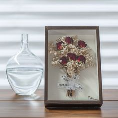 a glass vase with flowers in it next to a photo frame on a wooden table