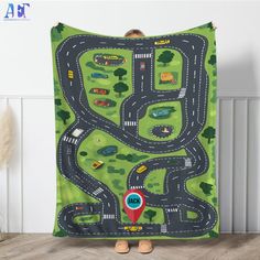 a child is holding up a blanket with a road and cars on it in front of a white wall