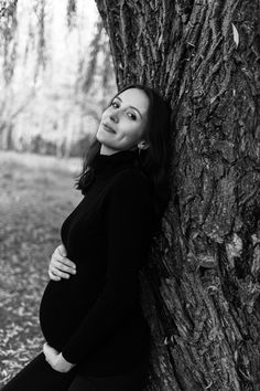 a pregnant woman leaning against a tree in black and white, posing for the camera