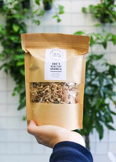 a person holding up a bag of granola in front of a potted plant