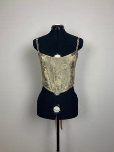 The classic corset is the perfect day to night top. The corset has internal boning, is fully lined with a poly charmeuse, and has a ribbon tying up the back. This corset has gold sliders, rings and grommets to pull the whole garment together. Made out of a gorgeous green - silver fabric with a gold metallic floral fabric. Utilize the size chart to pick the size that fits you best. Slightly adjustable due to corset back. THIS PIECE IS MADE TO ORDER - WILL SHIP UP TO TWO WEEKS AFTER ORDERING. Message if you have any questions. Night Tops, Silver Fabric, Ribbon Tie, Floral Fabric, Sliders, Gold Metal, Floral, Fabric