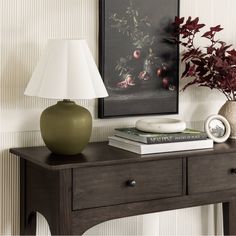 a table with a lamp, vase and books on it