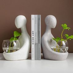 two white sculptures with plants in vases next to books