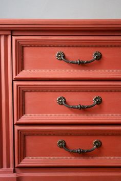 an orange dresser with brass handles and knobs on the top drawer is painted red