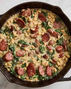 a skillet filled with sausage, spinach and macaroni in white sauce