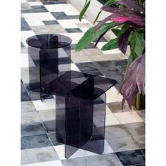 two black glass tables sitting on top of a checkered floor next to a potted plant