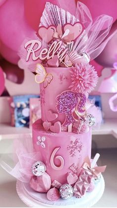 a pink cake with lots of decorations on it and balloons in the air behind it