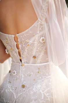 the back of a woman's wedding dress with flowers and beads on her shoulders