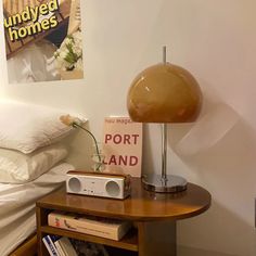 a small table with a lamp on top of it next to a bed and pillows