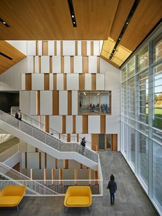 the inside of a building with stairs and people walking up to it, while two yellow chairs sit in front of them