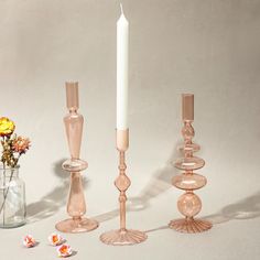 there are three candles and two vases with flowers in them on the table next to each other