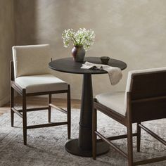 a small table with two chairs and a vase on the top, in front of a window