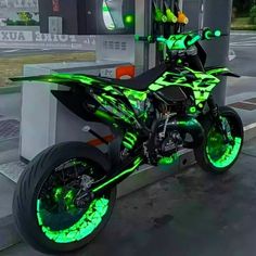 a green and black motorcycle parked in front of a gas station with its lights on