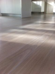 an empty room with hard wood flooring and white cabinets in the backround