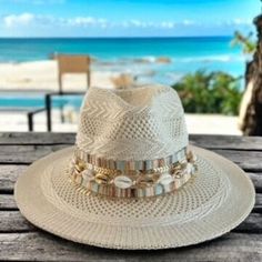 Calling all beach babes and summer queens!   Surf's up for the season with this on-trend panama hat, the perfect accessory to catch some rays and turn heads wherever you go.  This beauty features a classic cream-colored straw hat with a wide brim for maximum sun protection, accented with delicate seashells and gleaming gold chains for a touch of boho chic.  Whether you're strolling along the shoreline or sipping cocktails at a rooftop bar, this hat is sure to add a touch of whimsical flair to yo Casual White Hat Band For The Beach, Casual White Hat Band For Beach, Brimmed Panama Hat For Beach Season, Brimmed Panama Hat For Sunbathing On Vacation, Brimmed Panama Hat For Sunbathing In Beach Season, Vacation Panama Hat With Short Brim For Sunbathing, Short Brim Hat For Sunbathing And Vacation, Short Brim Hat For Sunbathing On Vacation, Brimmed Hat For Sunbathing Vacation