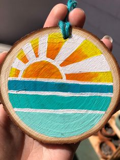 a hand holding a piece of wood that has been painted with the sun and ocean