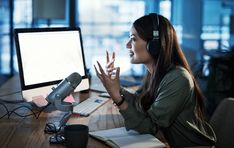 a woman wearing headphones sitting at a desk with a computer and microphone in front of her