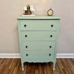 a green dresser sitting on top of a hard wood floor next to a white wall