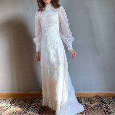 a woman standing in front of a wall wearing a white dress