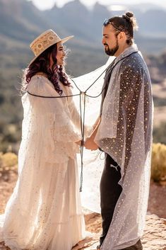 a man and woman standing next to each other on top of a mountain holding hands