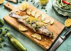 a fish on a cutting board with lemons and zucchini