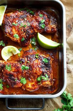 two pieces of chicken covered in sauce and garnished with cilantro and lime