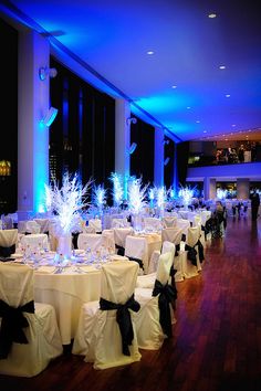 a banquet hall decorated with white tablecloths and black sashes, lit by blue lights