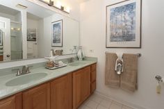 a bathroom with double sinks and large mirror above it's counter top, along with two framed pictures on the wall