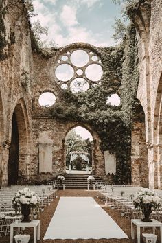 an outdoor ceremony setup with white flowers and greenery on the aisle, surrounded by stone arches