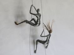 two wire sculptures are hanging from strings on the wall, one is holding a plant