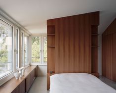 a bed sitting next to a window in a room with lots of wooden cabinets and windows