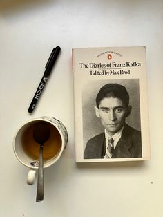 a cup of tea next to a book with a spoon on it and a pen