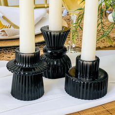 three black candle holders sitting on top of a white table cloth next to wine glasses