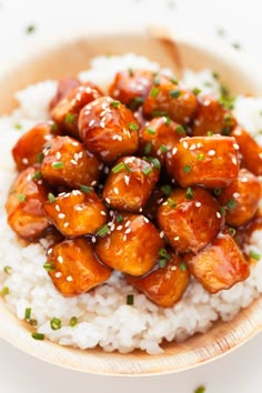 a wooden bowl filled with rice covered in chicken and sesame seeds on top of it