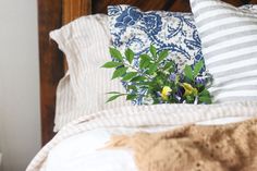 a bouquet of flowers sits on the edge of a bed with striped pillows and blankets