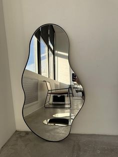 a mirror sitting on top of a white wall next to a chair and table in front of a window