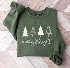 Get into the holiday spirit with our Merry & Bright Olive Green Christmas Tree Crewneck! This cozy, festive sweater combines a classic color with a cheerful Christmas design, making it a standout piece for the season. Key Details: Color: Classic olive green Design: Eye-catching Christmas tree graphic adorned with sparkling decorations and a "Merry & Bright" message Material: Soft and durable cotton for maximum comfort Fit: Relaxed, classic crewneck style for easy layering Neckline: Ribbed crew n Hunter Green Christmas, Christmas Shirts For Women, Idee Cricut, Merry Bright Christmas, Cute Shirt Designs, Christmas Crewneck, Vinyl Shirts, Diy Cricut, Green Christmas Tree