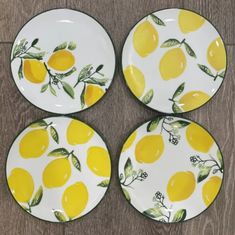 four plates with yellow lemons painted on them sitting on a wooden tablecloth covered floor