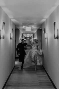 a man and woman walking down a long hallway with lights on either side of them