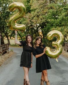 two women holding up gold balloons in the shape of numbers 3 and 3 on a road