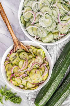 two bowls filled with cucumbers and onions next to a wooden spoon on a marble surface