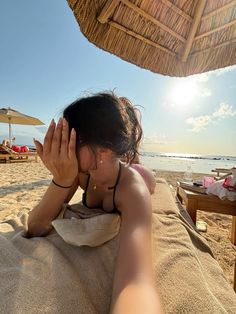 a woman laying on top of a sandy beach next to an umbrella over her head